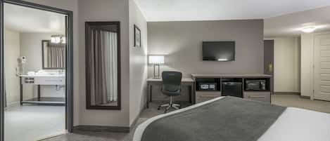 Habitación de hotel con cama, escritorio, silla, televisión y baño con espejo, lavamanos y toallero.