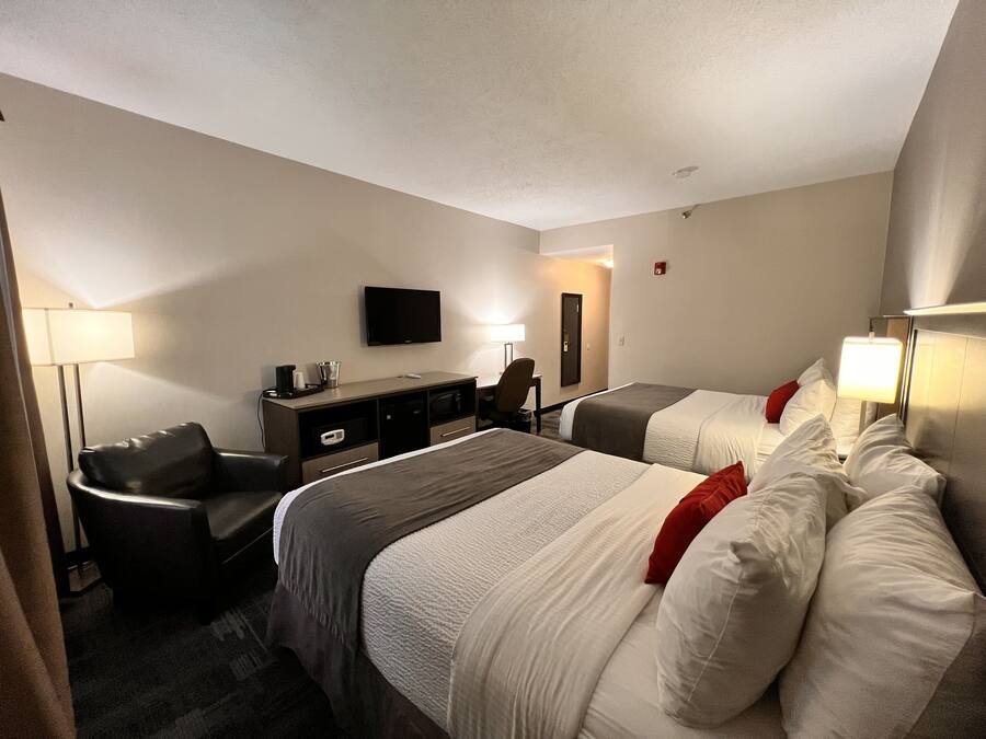 Une chambre d’hôtel avec deux lits, un bureau, une chaise, une télévision et une lampe.