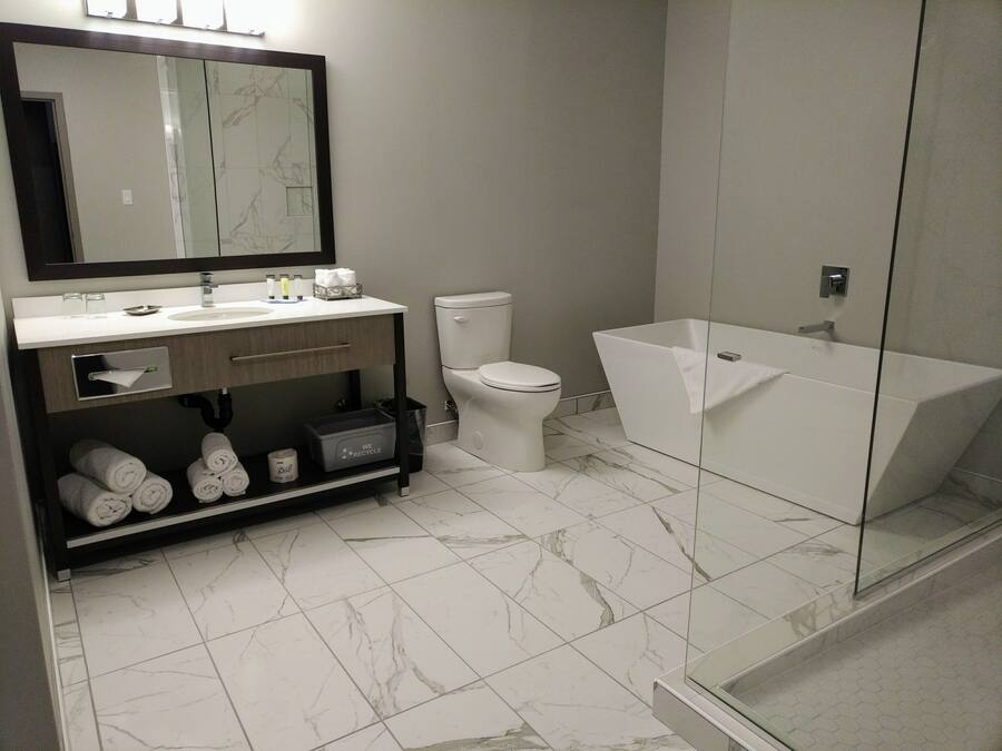 A modern bathroom with a marble-tiled floor, a white toilet, a white sink, a mirror above the sink, and a glass-enclosed shower area.