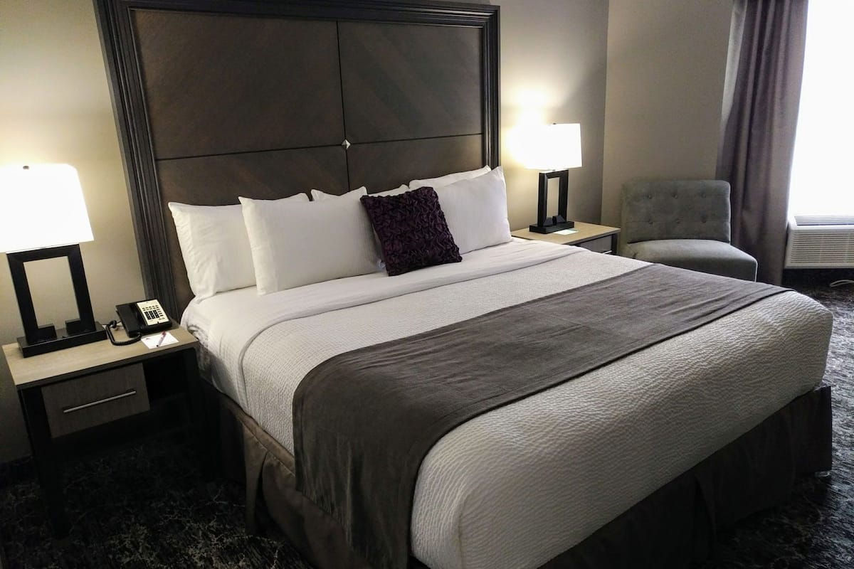 A hotel room with a large bed, two bedside tables with lamps, a chair, and a window with curtains.