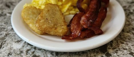 Un plato con huevos revueltos, tocino y patatas ralladas sobre una encimera de granito.