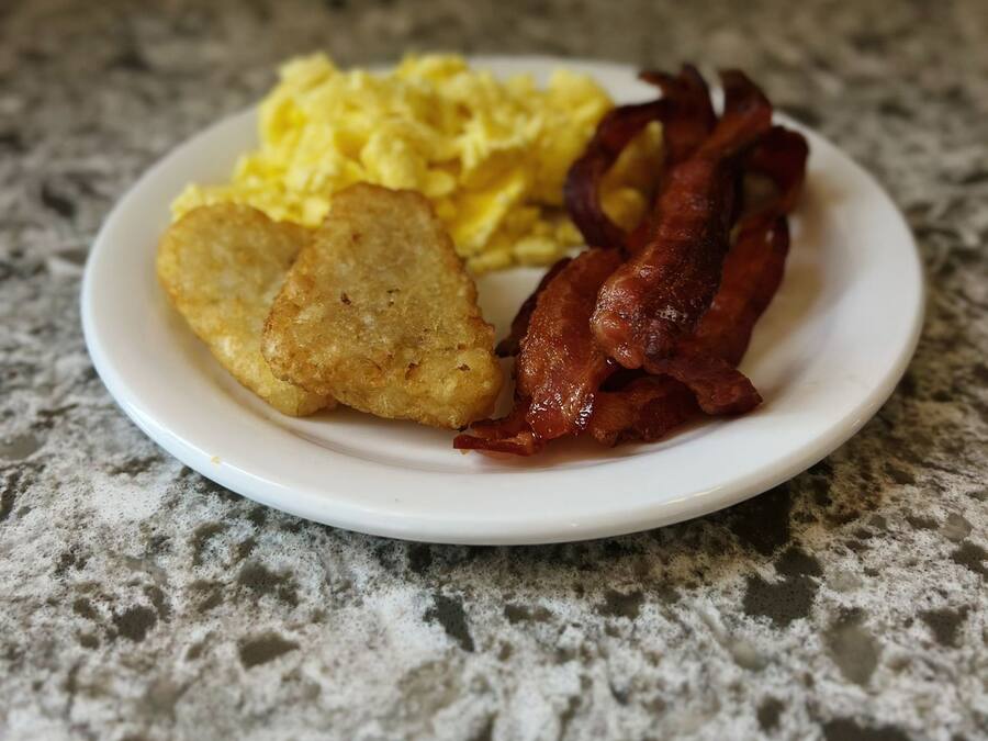 A plate with scrambled eggs, bacon, and hash browns on a granite countertop.