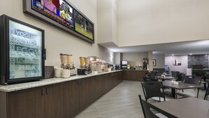 Et hotel lobby med et morgenmadsbord, et køleskab med yoghurt og mælk, og et fjernsyn der viser nyheder.