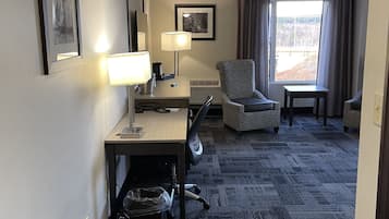 A hotel room with a desk, chair, lamp, and a large window with curtains.