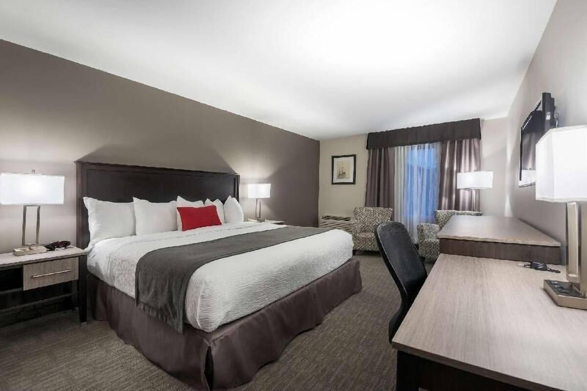 A hotel room with a large bed, bedside tables, a desk, a chair, and a lamp.