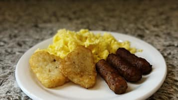 A plate with scrambled eggs, hash browns, and sausages on a granite countertop.