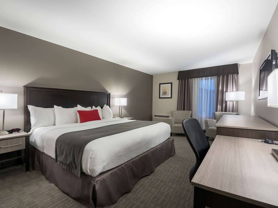 A hotel room with a large bed, a desk, a chair, and a TV.