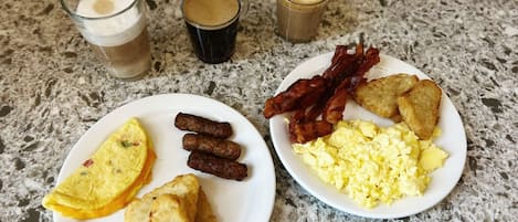 A breakfast plate with eggs, bacon, sausages, and toast, and two glasses of coffee on a granite countertop.
