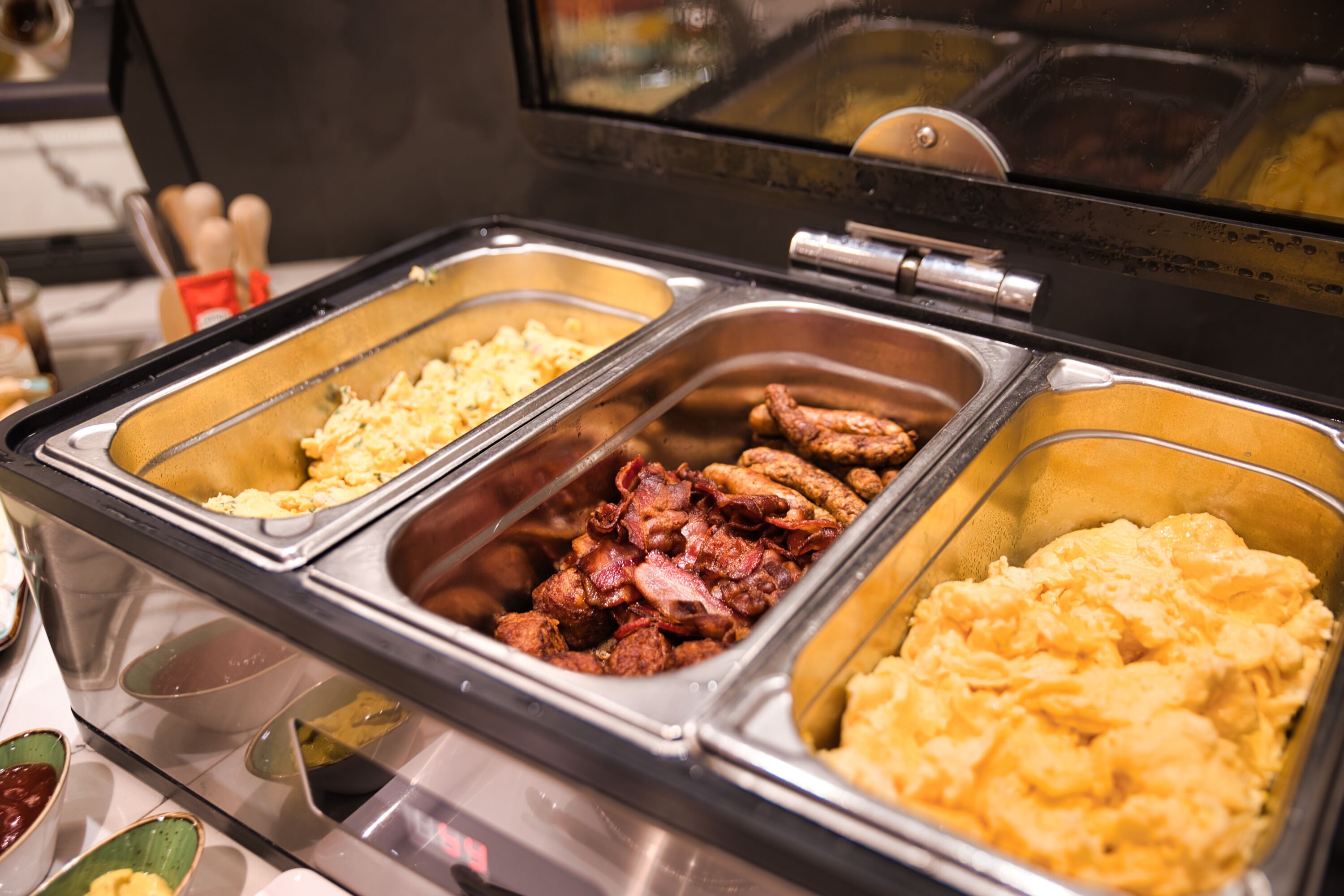 Ein reichhaltiges Buffet mit verschiedenen Speisen, darunter Rührei, Speck und Kartoffelpüree.