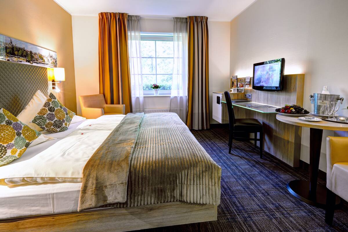 Une chambre d’hôtel avec un lit, un bureau, une télévision et une fenêtre avec des rideaux.