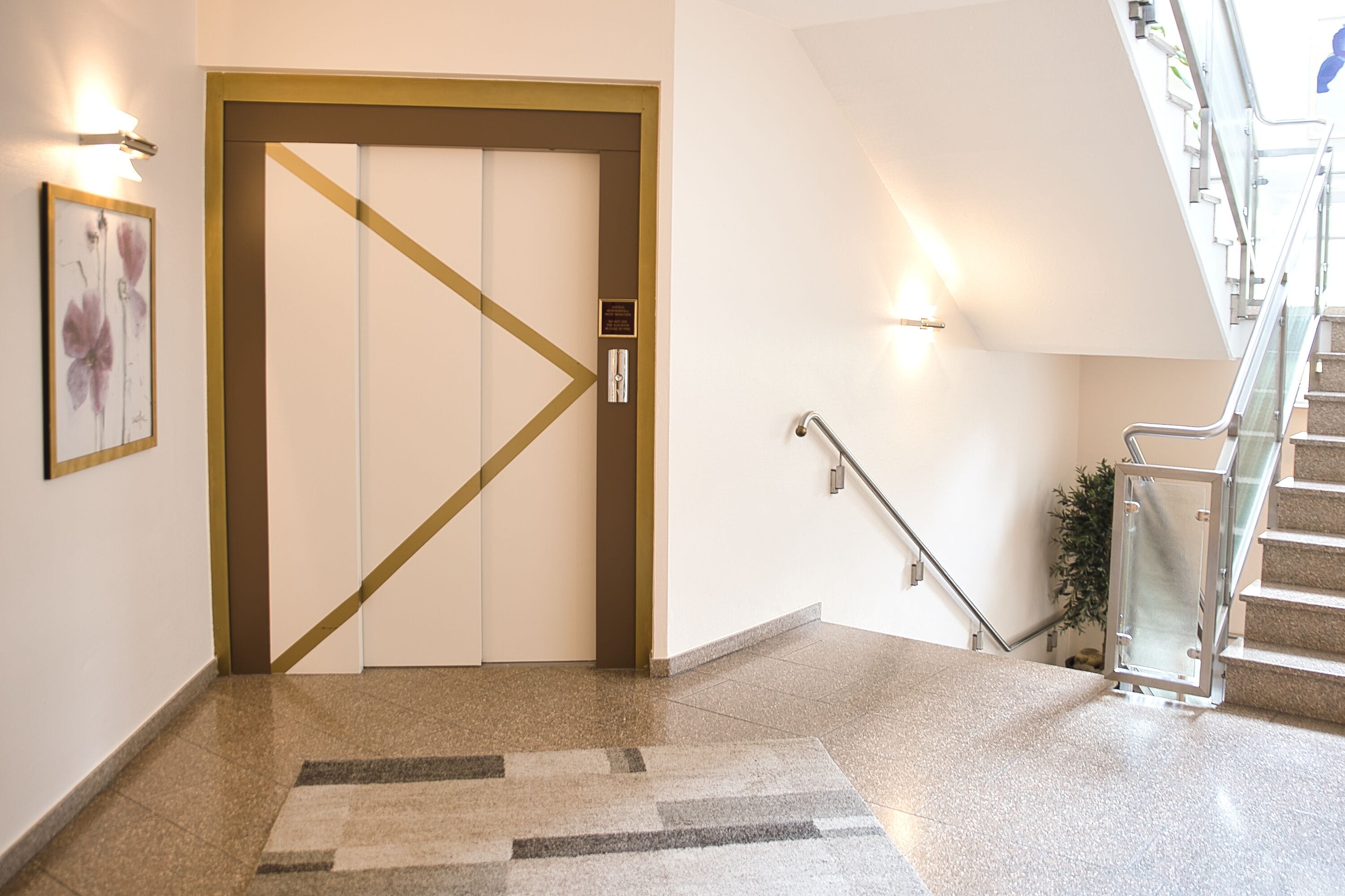 A hotel lobby with a glass staircase, a carpeted floor, and a door with a diagonal stripe design.