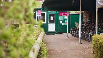 A bicycle rental station with a green shelter, a sign indicating personal use, and a row of bicycles.