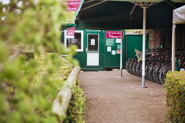 Un point de location de vélos doté d’un abri vert, d’un panneau indiquant qu’ils sont réservés à un usage personnel, et d’une rangée de vélos.