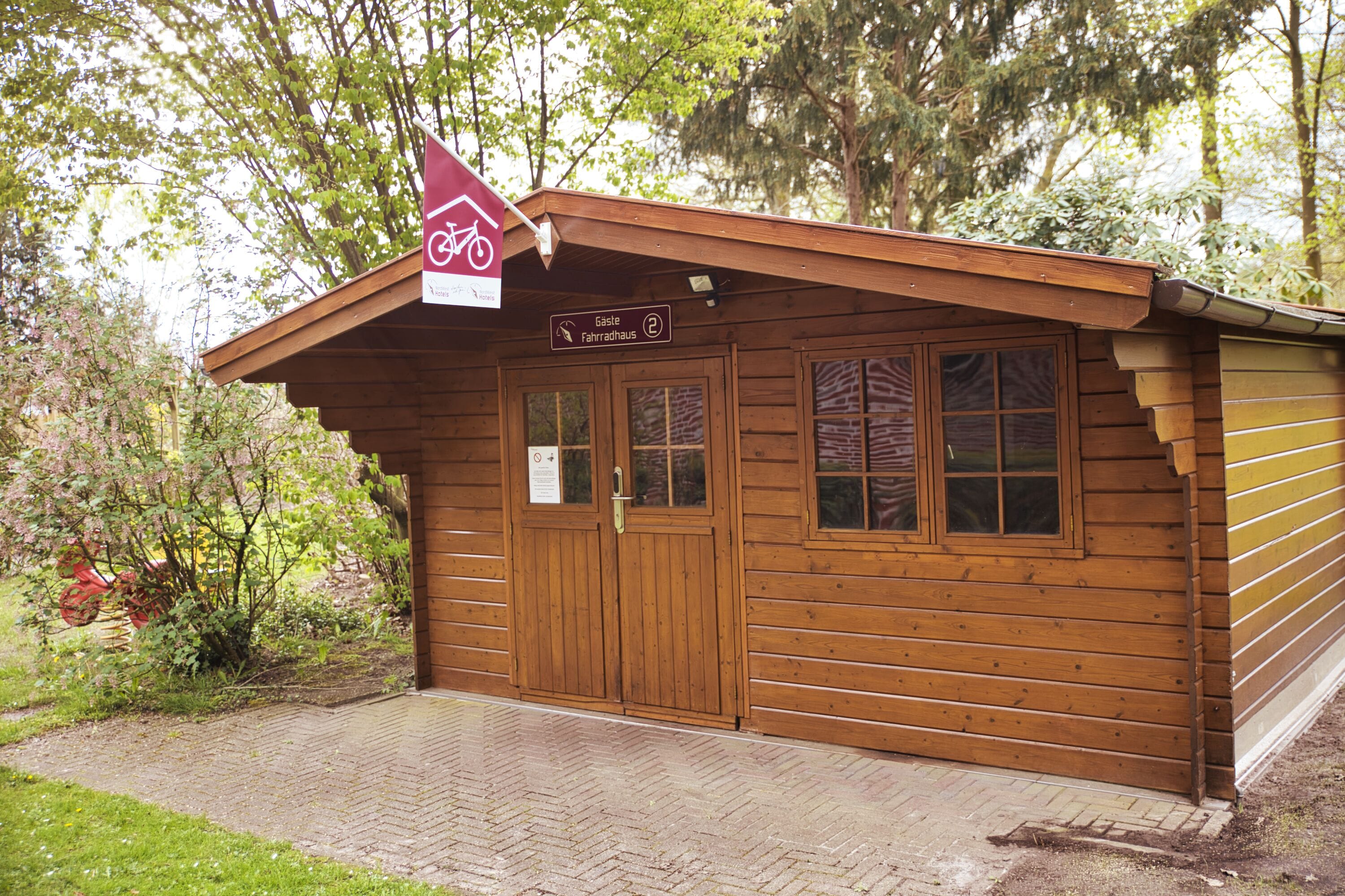 Una cabaña de madera con un letrero que indica que es una casa de huéspedes, una puerta, ventanas y un acceso pavimentado.