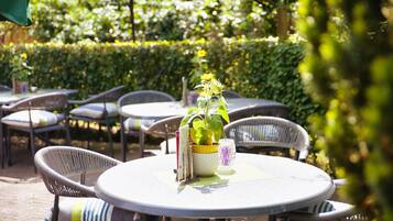 An outdoor seating area with round tables and wicker chairs, a potted plant, and a glass on the table.