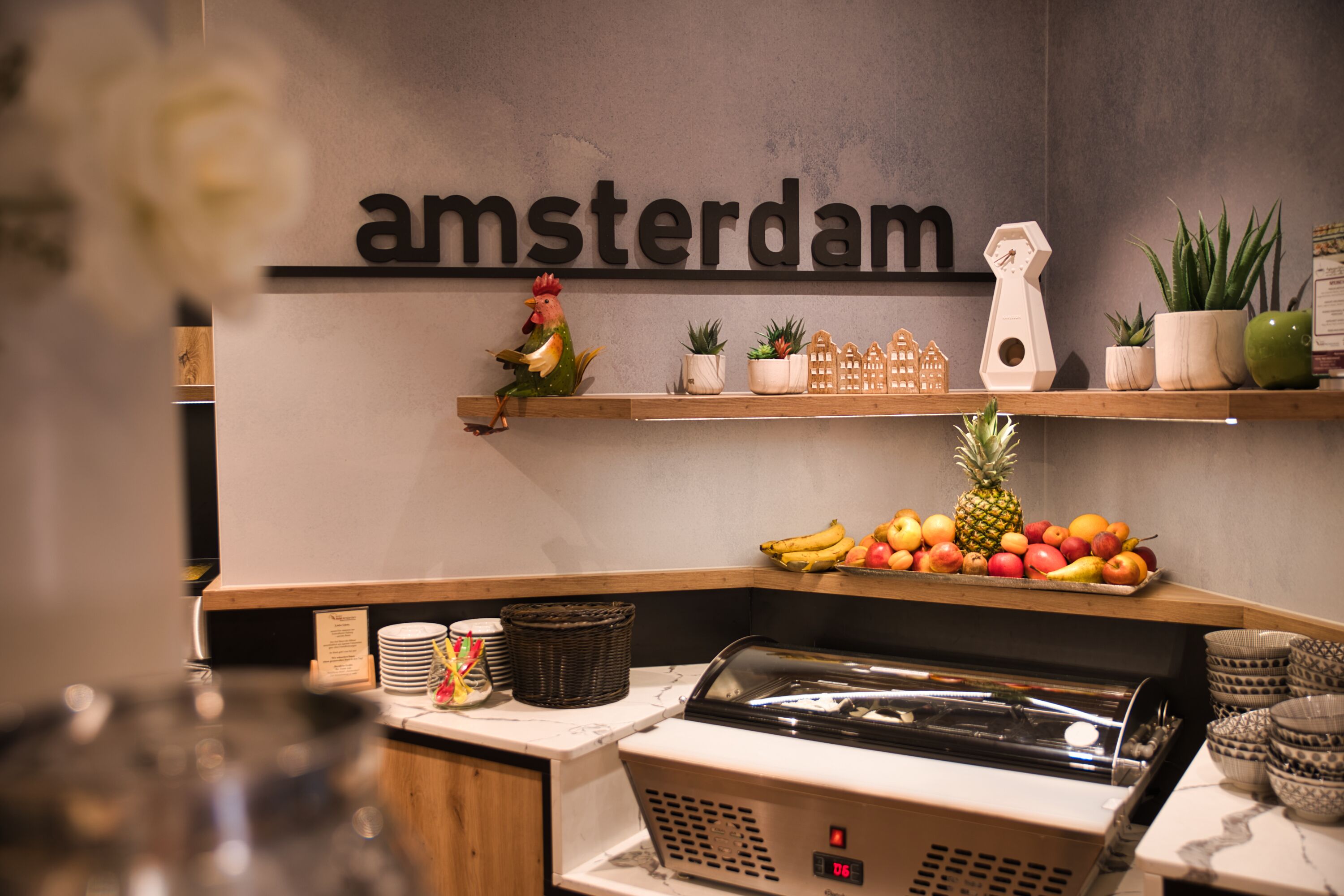 Et tekøkken med et skilt der står 'amsterdam', et frugtudvalg og en kaffemaskine.