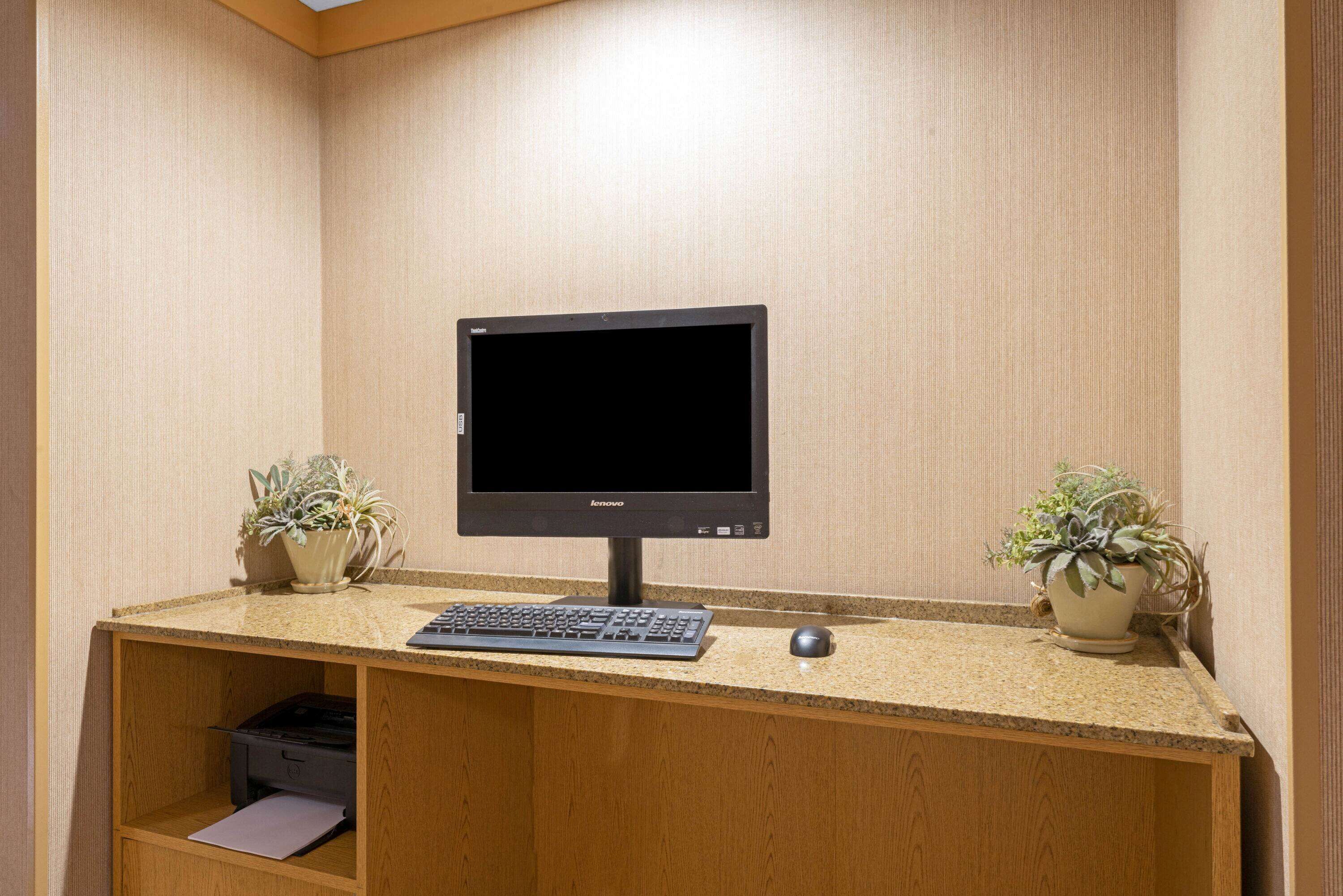 Ein Computertisch mit Monitor, Tastatur und Maus. Auf beiden Seiten des Tisches stehen je ein Blumentopf.