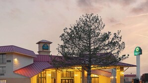 Een hotel met een grote boom ervoor, een rood dak en een bord met Quinta Inn & Suites.