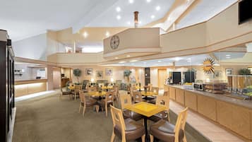 Un hall d’hôtel spacieux comprenant plusieurs espaces de restauration, un comptoir d’accueil et une cuisine visible au fond.