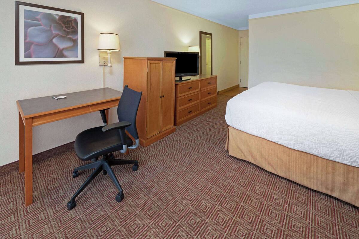 Ein Hotelzimmer mit einem Bett, einem Schreibtisch mit Stuhl, einem Fernseher, einem Kleiderschrank und einer Lampe.