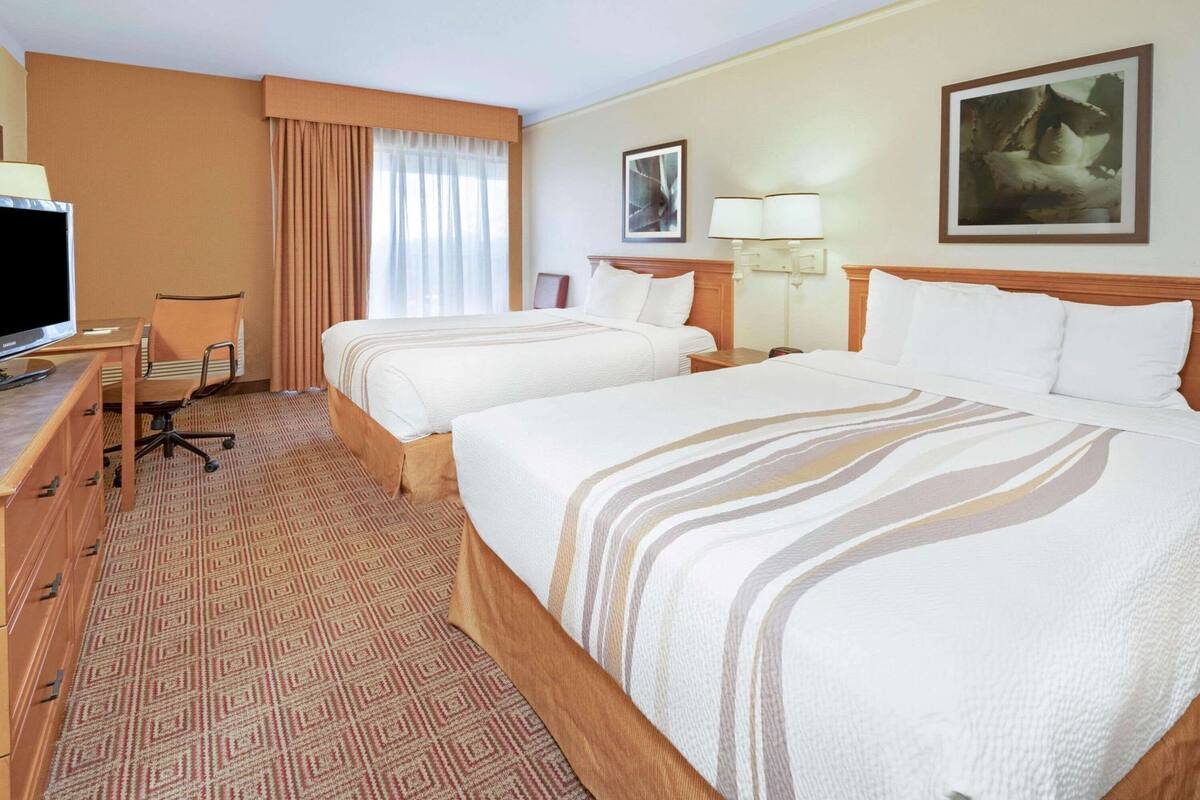 Ein Hotelzimmer mit zwei Betten, einem Schreibtisch mit Fernseher, einem Sessel und einem gemusterten Teppich.
