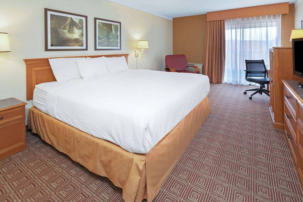 Ein Hotelzimmer mit einem großen Bett, einem Schreibtisch, einem Sessel, einem Fernseher und zwei gerahmten Bildern an der Wand.