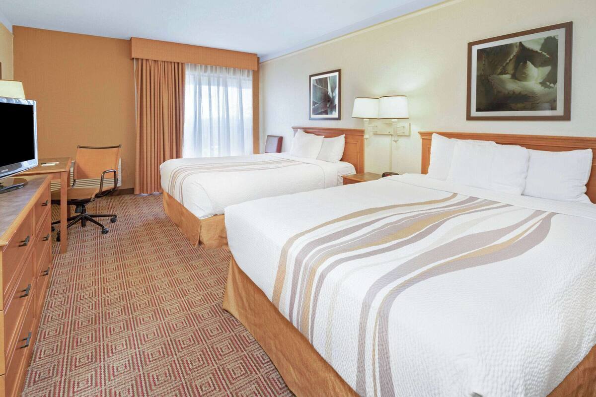 Ein Hotelzimmer mit zwei Betten, einem Schreibtisch mit Computer, einem Stuhl und einem Fernseher.