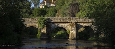 Un puente de piedra con tres arcos sobre un río, que conduce a un edificio histórico con una torre.