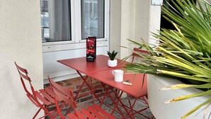 A red metal table and chairs set against a white wall, with a potted plant to the right and a sign on the wall. - ibis Alencon (Alencon)