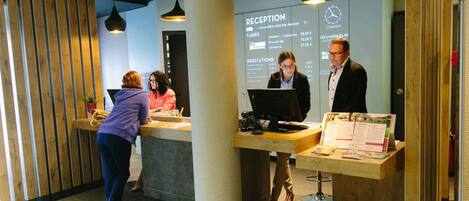 A reception desk with a computer, a wooden column, and a wall with a sign listing room rates and amenities.