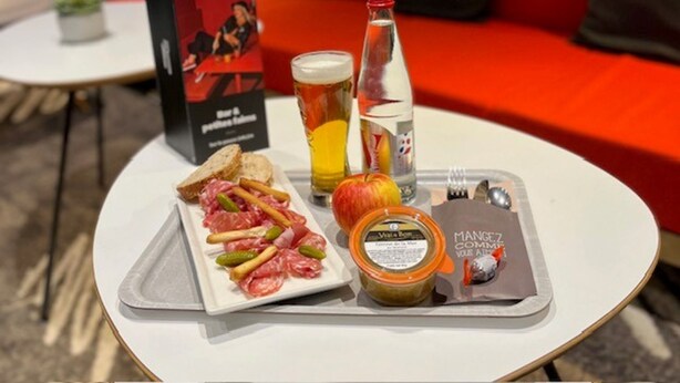A table with a tray of food, a bottle of water, a glass of beer, and a menu. - ibis Alencon (Alencon)