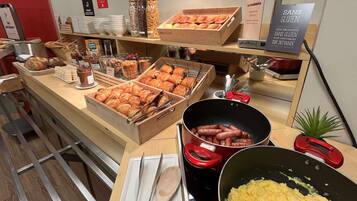 A buffet with various food items, including pastries, sausages, and scrambled eggs.
