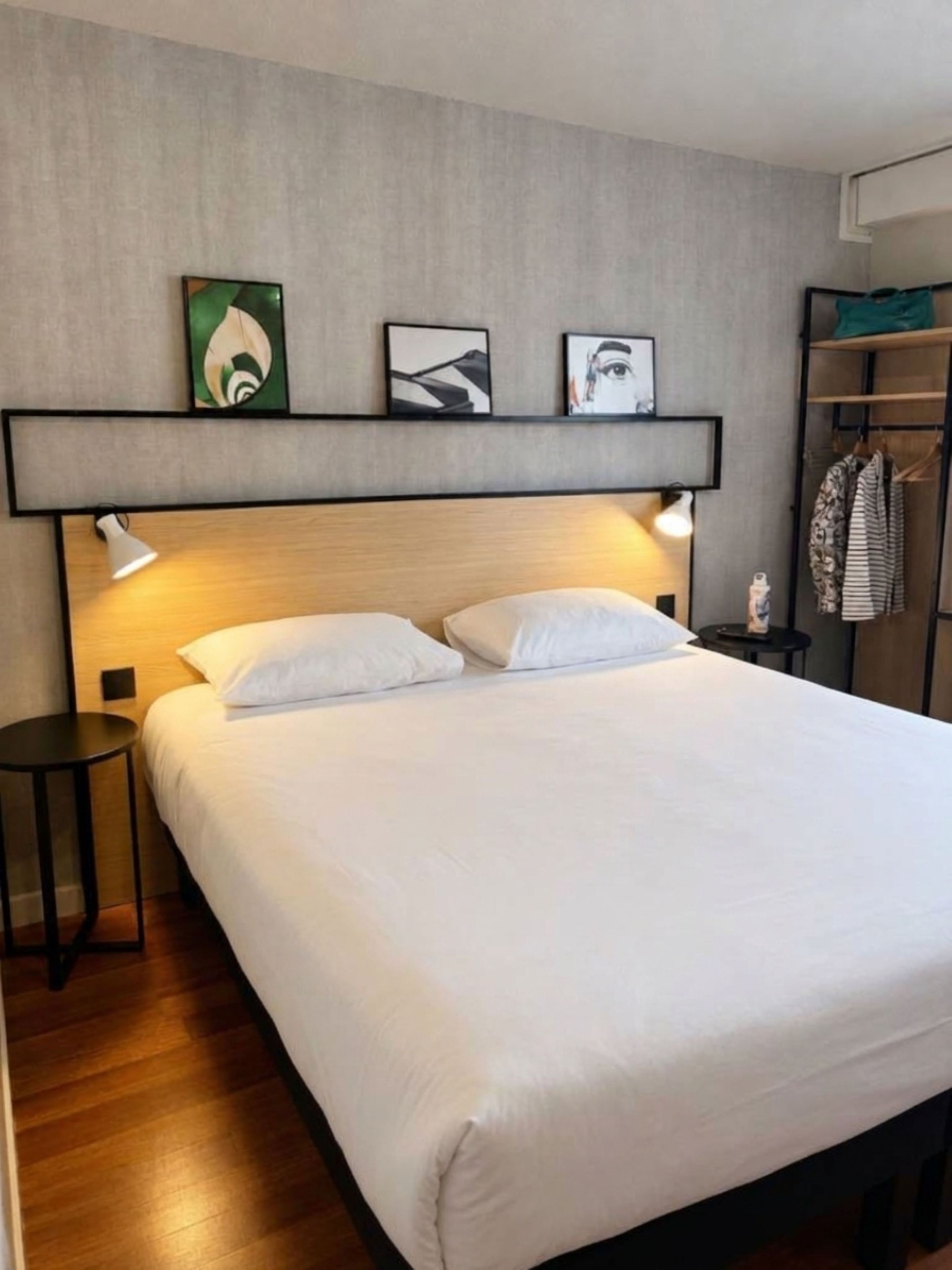 A neatly made bed with white linens, a bedside lamp, and a small round table. There are three framed artworks on the wall above the bed.