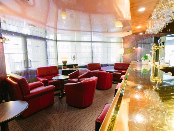 Un hall de hotel con asientos de cuero rojo, una zona de bar y ventanas amplias.