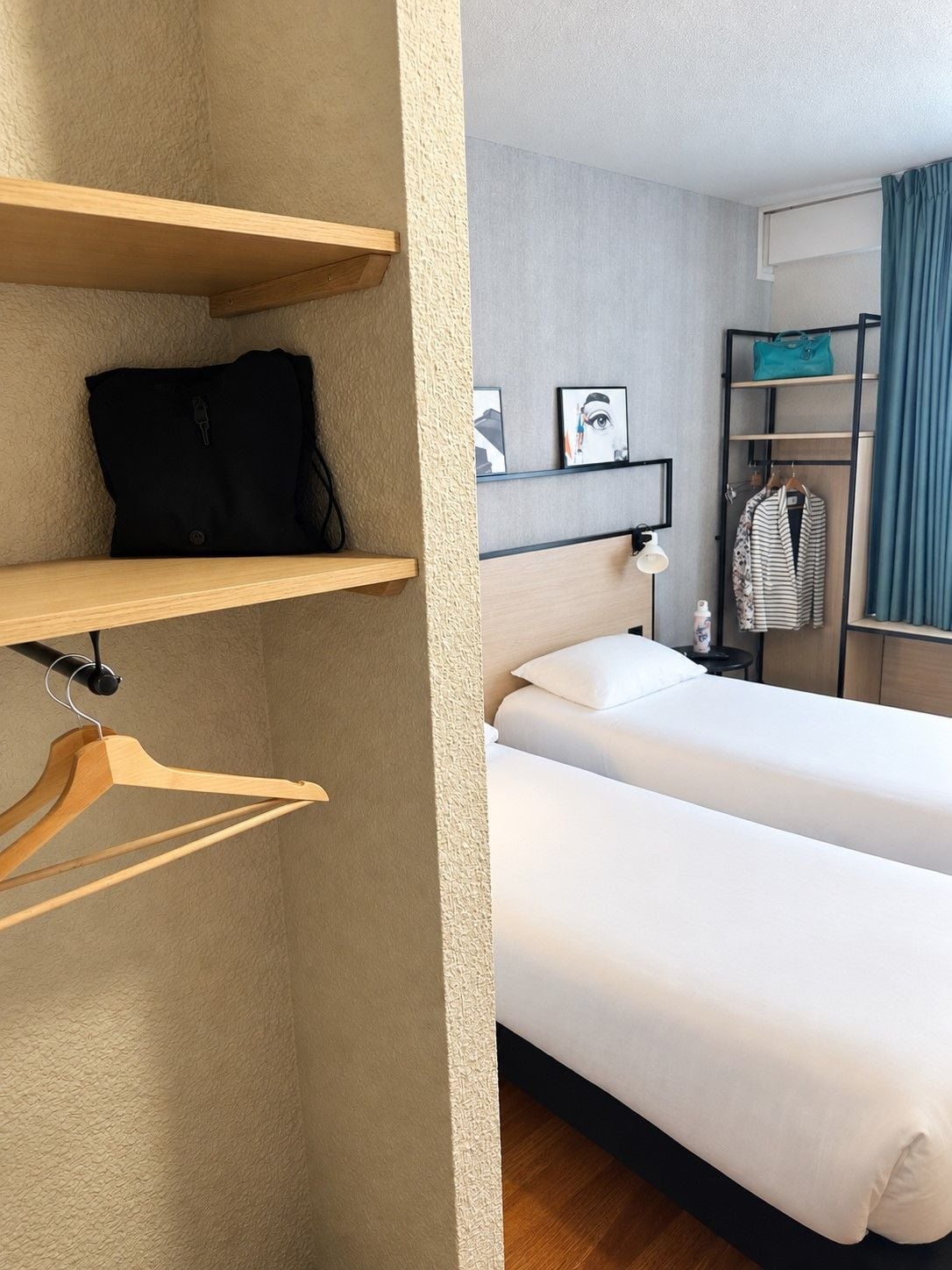 Hotelkamer met een bed, een garderobe, een kapstok en een plank met een tas en een foto.