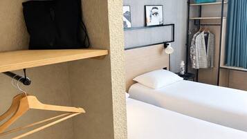 Hotelkamer met een bed, een garderobe, een kapstok en een plank met een tas en een foto.