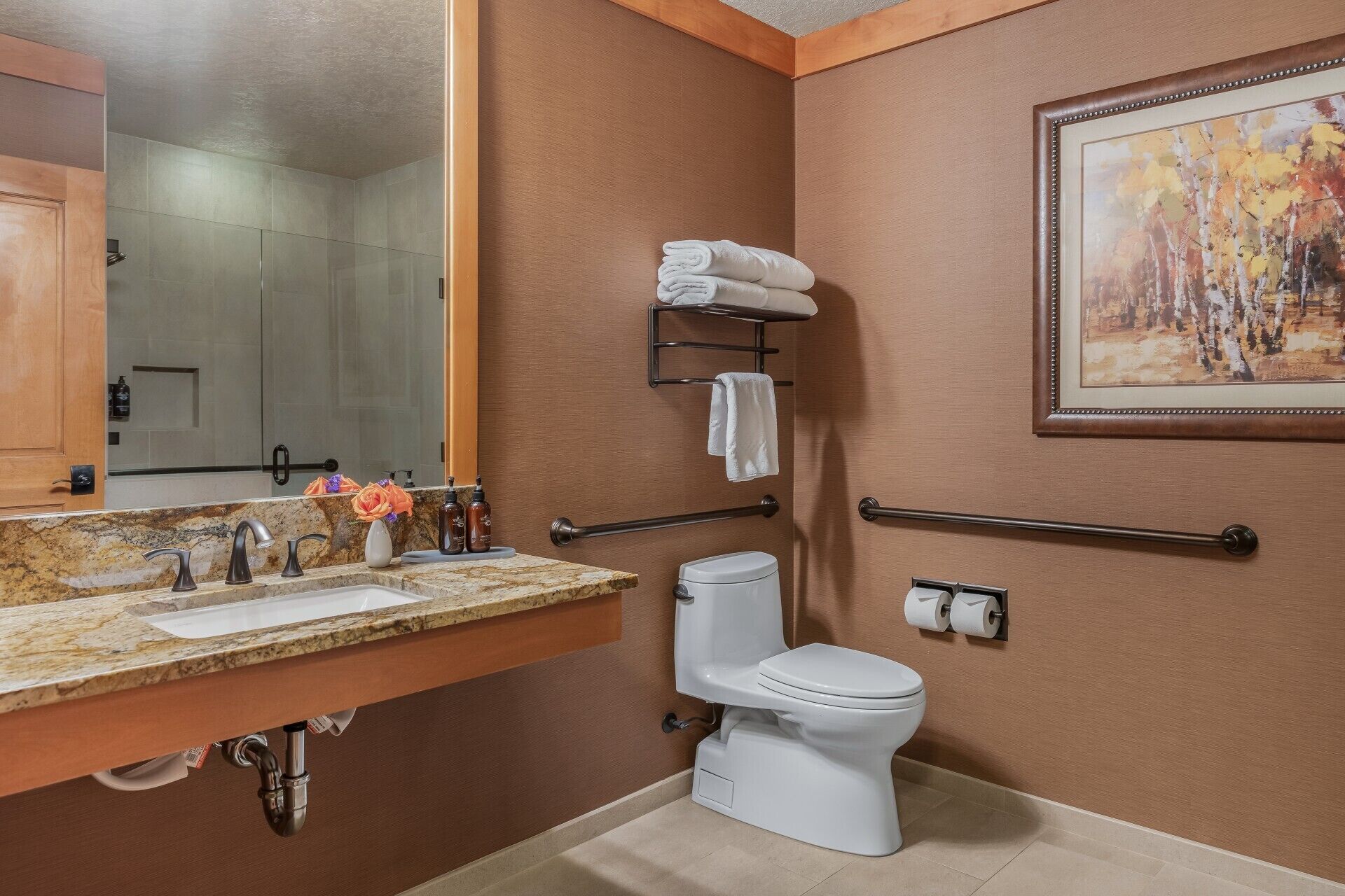 Ein Badezimmer mit Marmorwaschbecken, Toilette, Haltegriff und einem Bild an der Wand.