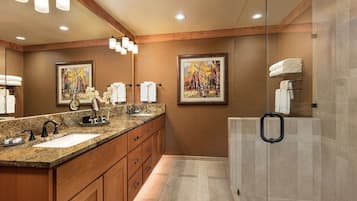Un baño moderno con dos lavamanos, armarios de madera y mampara de ducha de vidrio.