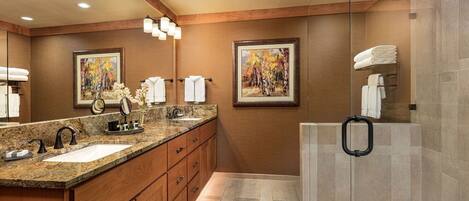 A modern bathroom with two sinks, wooden cabinets, and a glass shower enclosure.