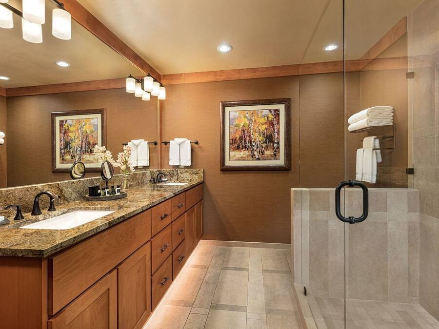 Un baño moderno con dos lavamanos, armarios de madera y mampara de ducha de vidrio.
