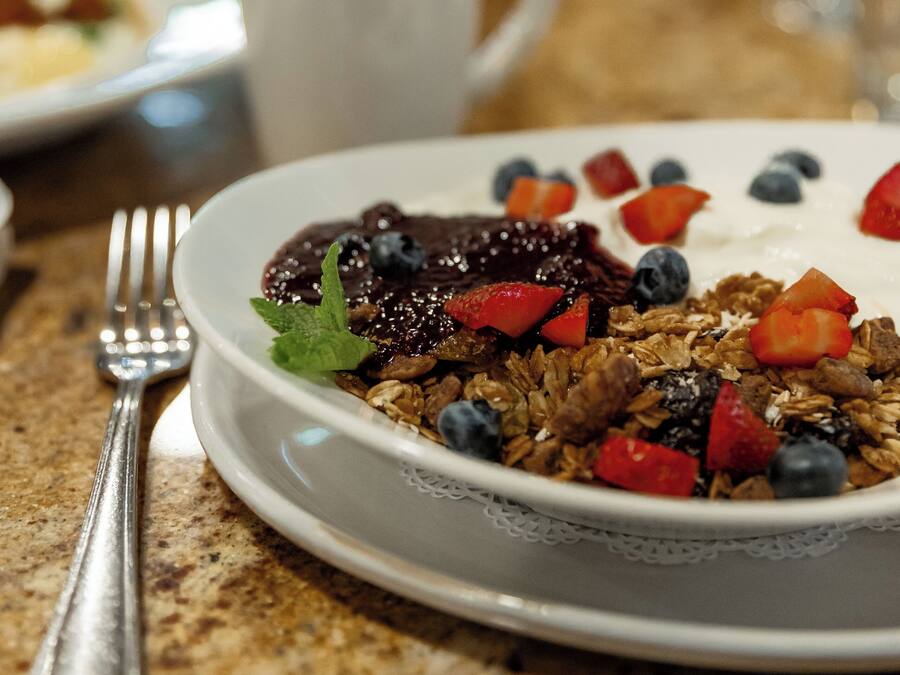 A breakfast plate with granola, yogurt, blueberries, strawberries, and a mint leaf on a table.