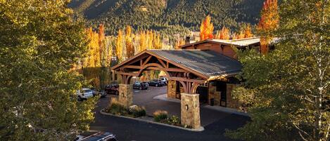 A lodge with a covered parking area, stone pillars, and a mountainous backdrop.