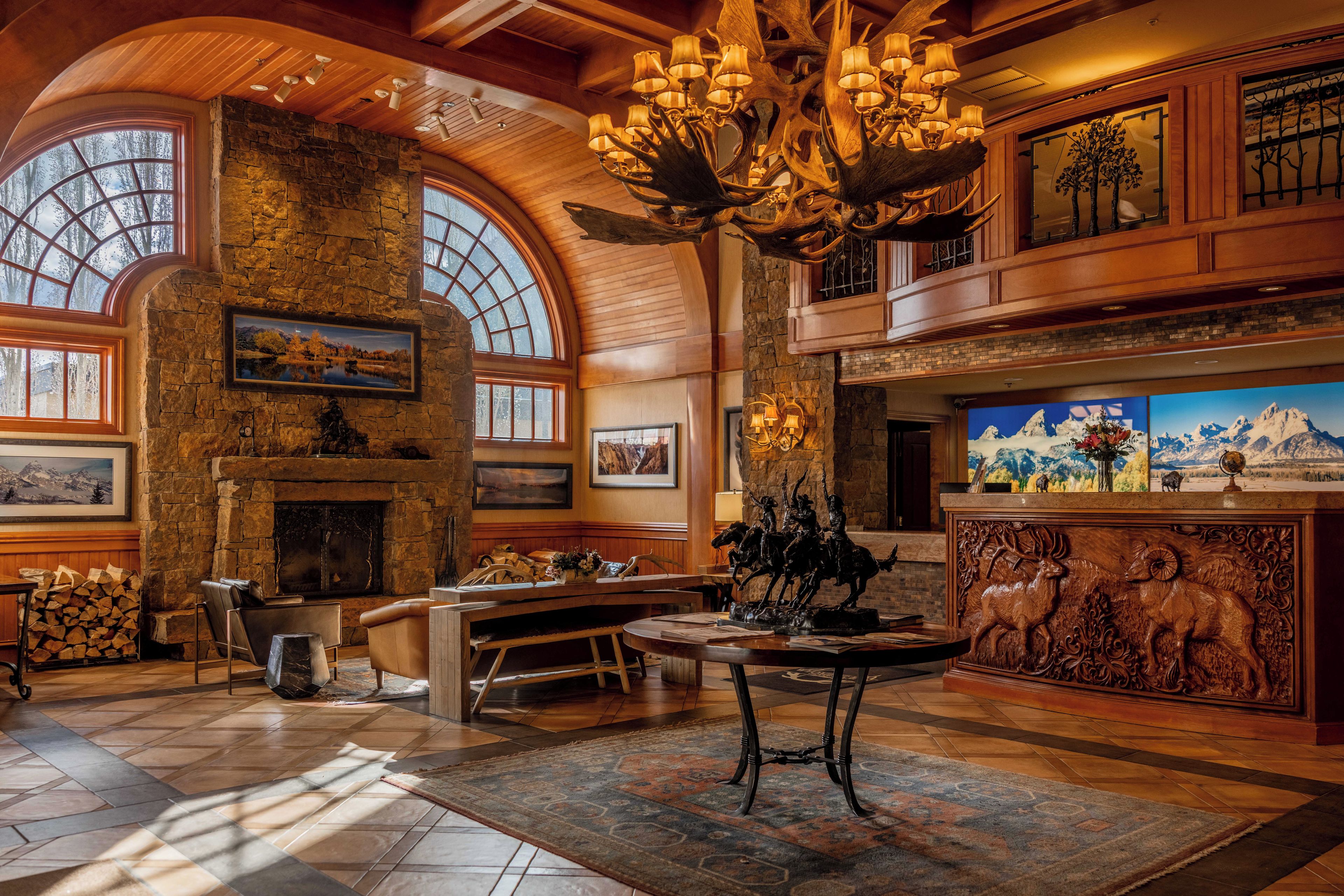 A spacious lobby with a stone fireplace, wooden ceiling, and a large chandelier.