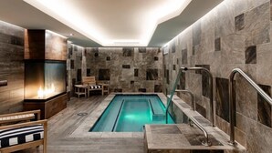 A modern indoor pool area with a stone wall, a fire feature, and a seating area. - The Wyoming Inn of Jackson Hole (Jackson)