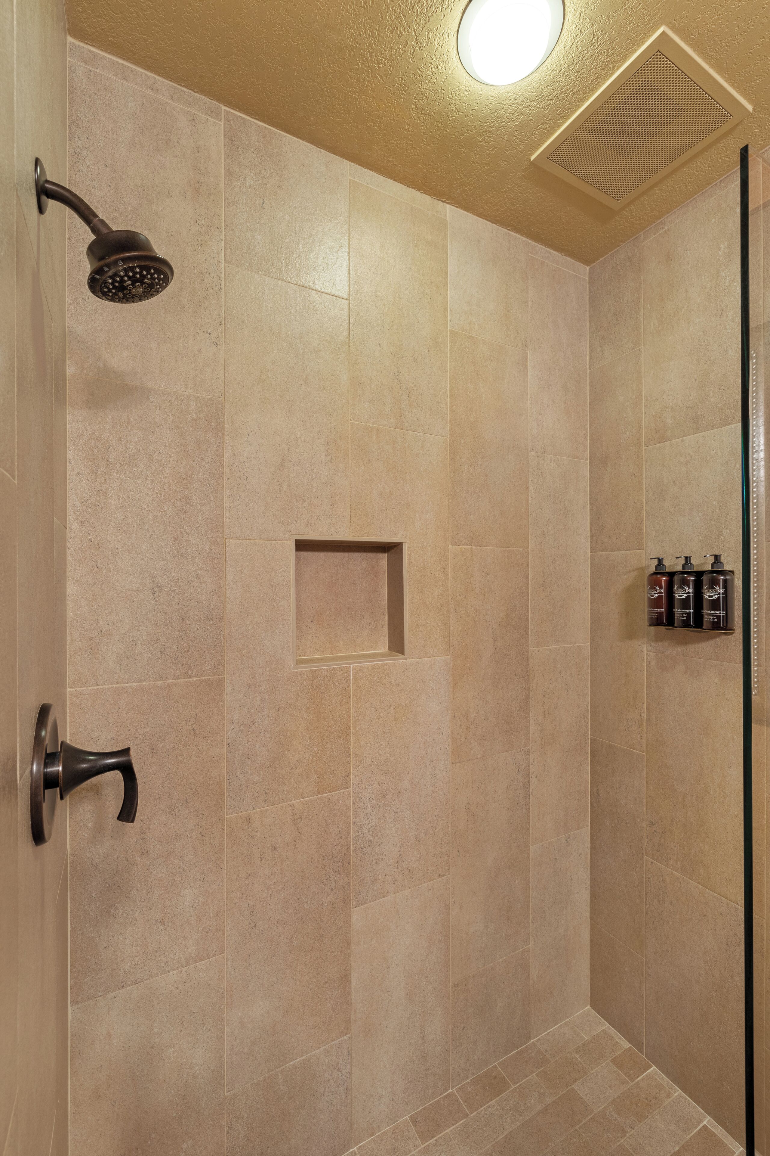 A shower with a handheld showerhead, a small shelf, and a wall-mounted soap dispenser.