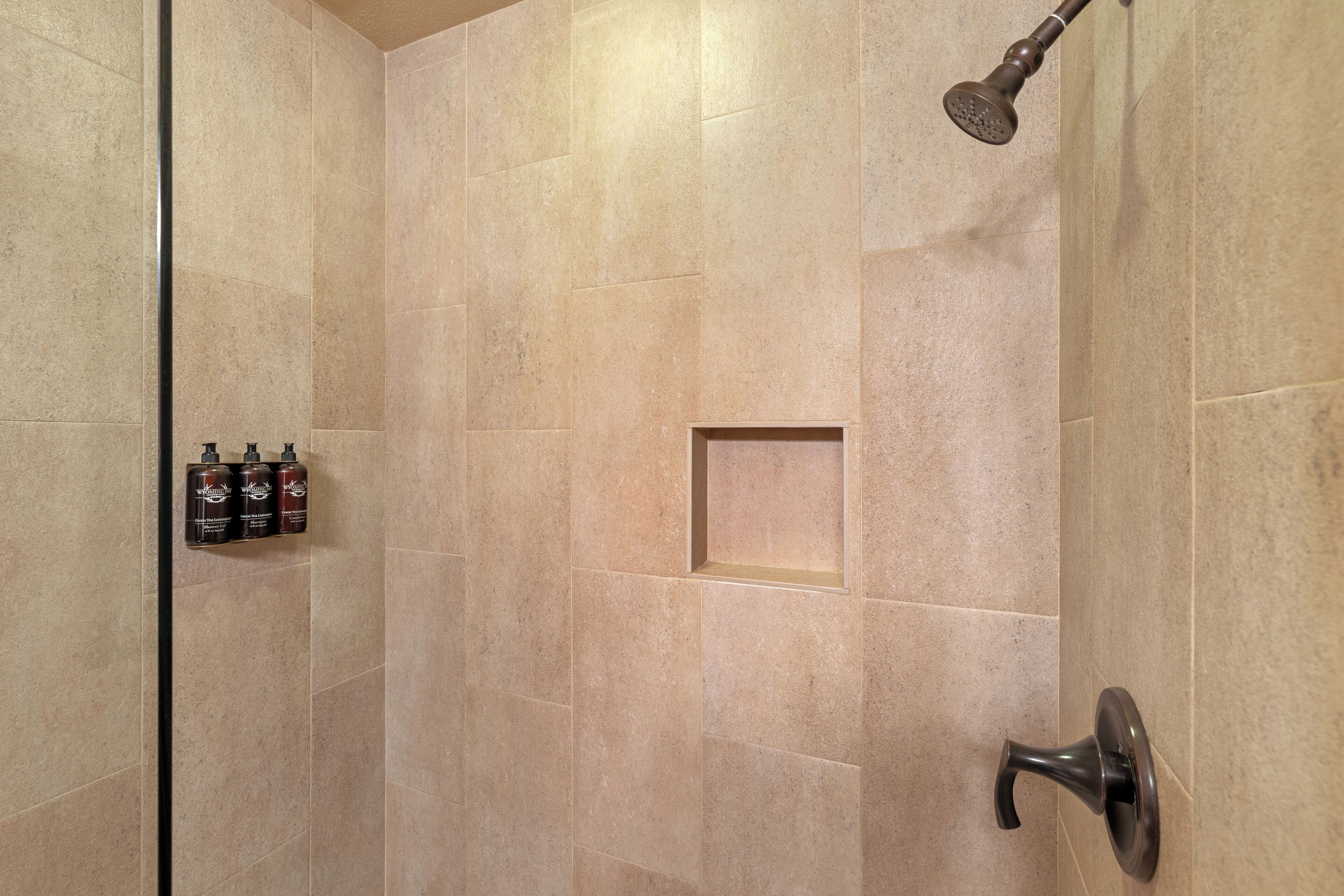 A shower with beige tiles, a handheld showerhead, and a soap dispenser mounted on the wall.