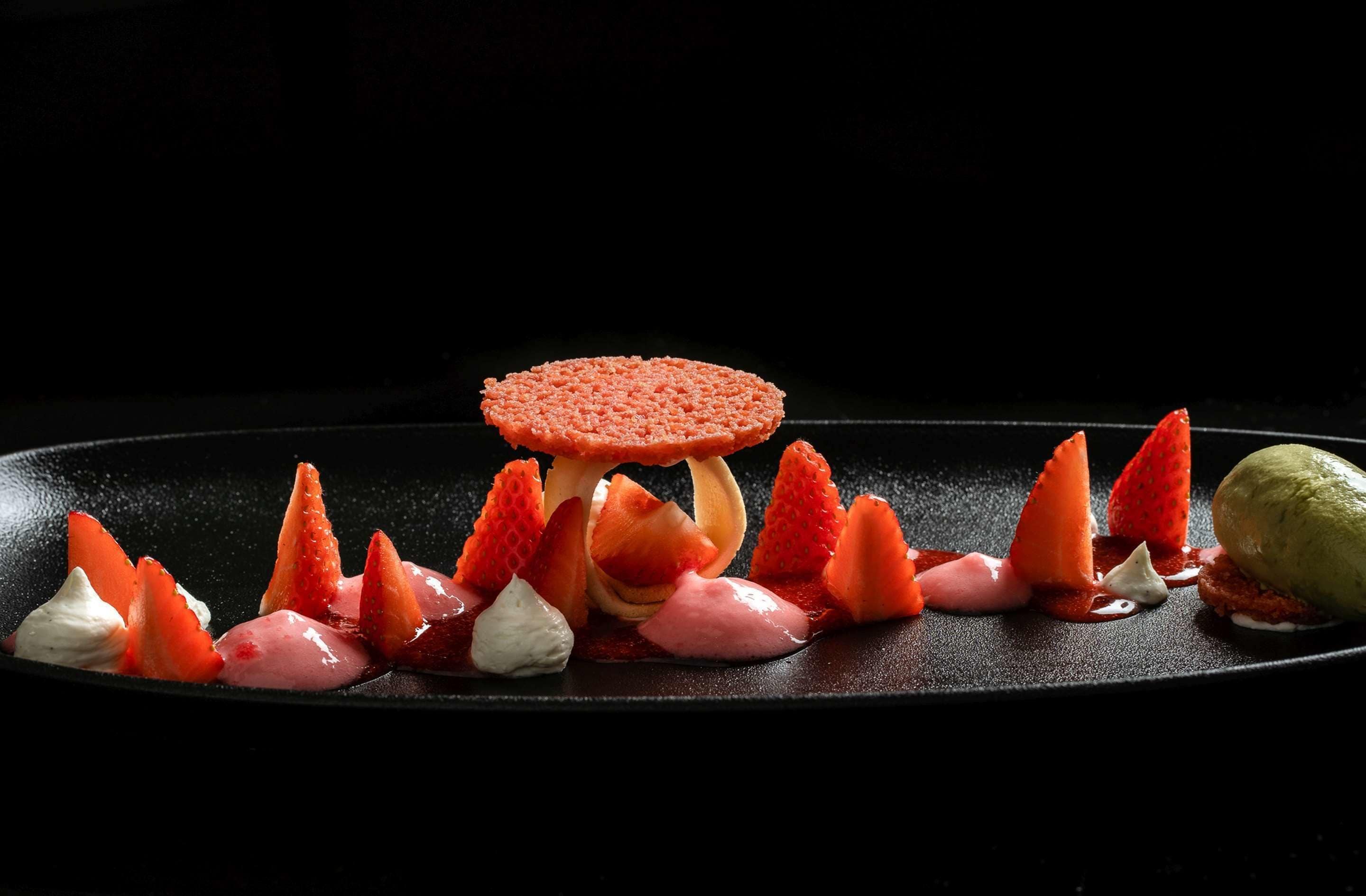 Une assiette de dessert avec des fraises, une boule de glace et un objet rond à la texture particulière.