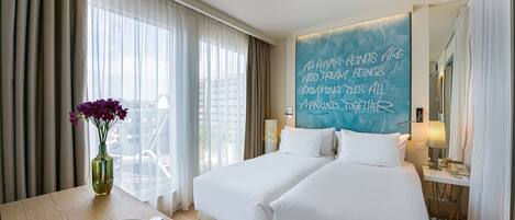 A hotel room with two beds, a dining table with breakfast, a vase of flowers, and a motivational quote on the wall.