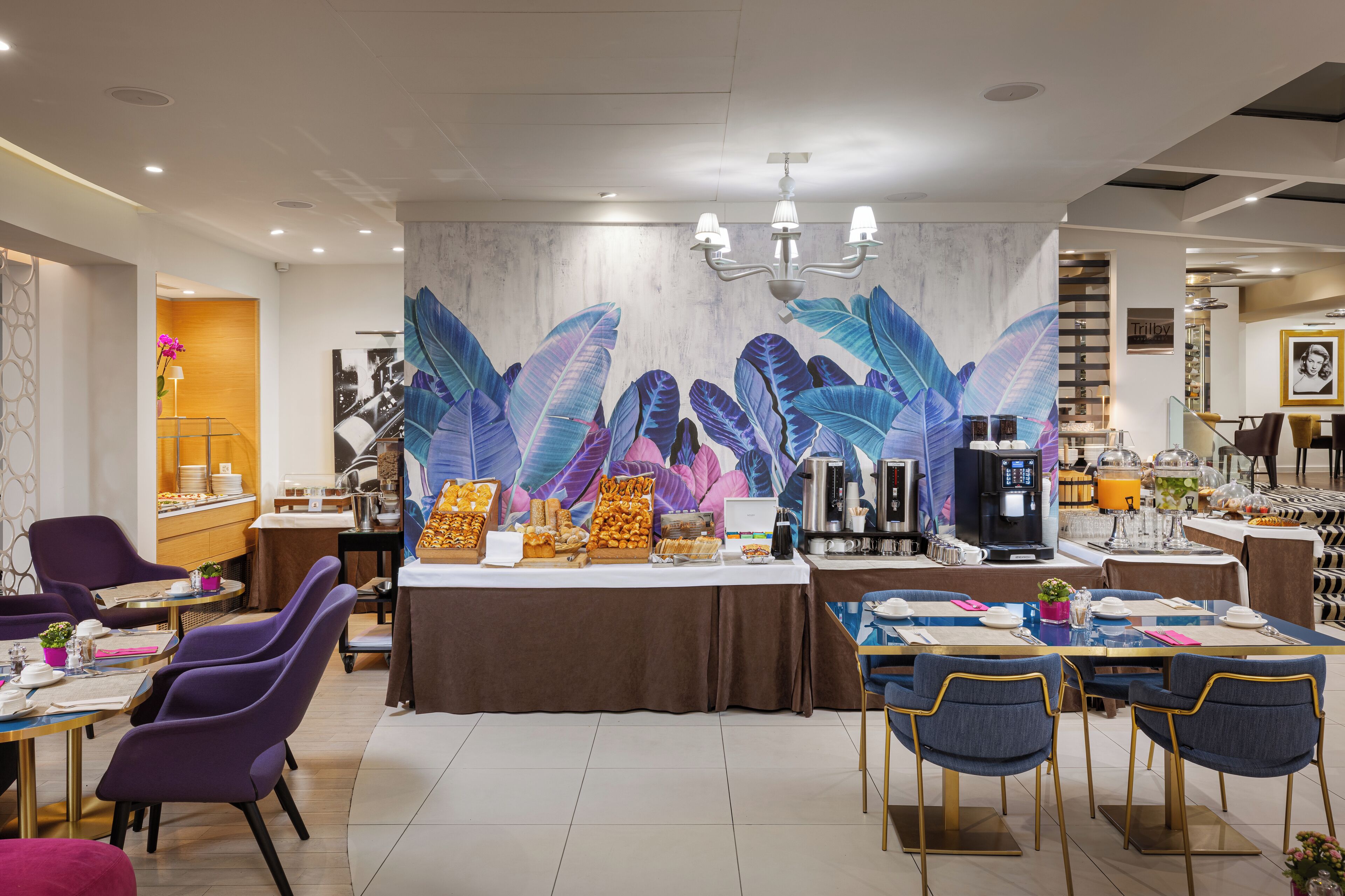 A modern dining area with purple chairs, a buffet table with various food items, and a large decorative wall with leaf patterns.