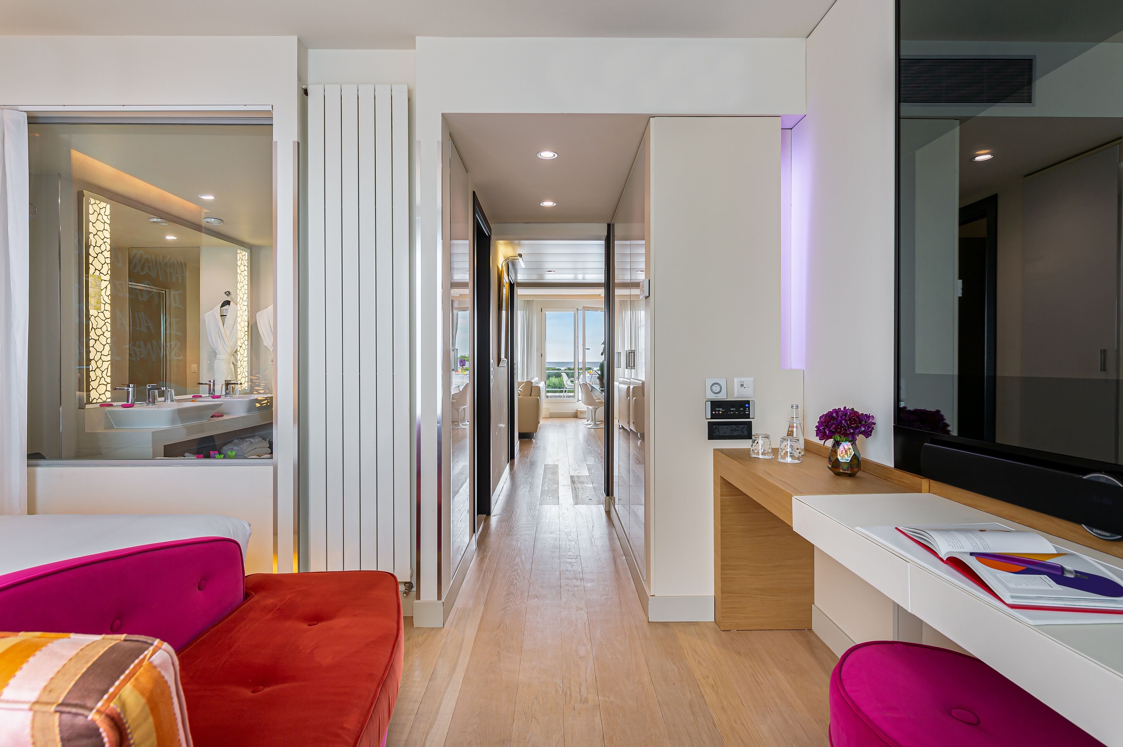 A modern hotel room with a bright, well-lit hallway leading to a bathroom and a living area.
